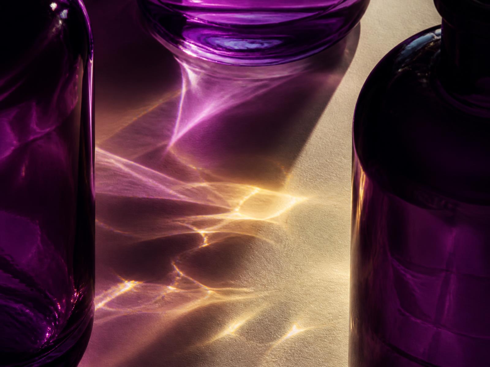 Macro photograph of violet glass bottles refracting gold and purple light